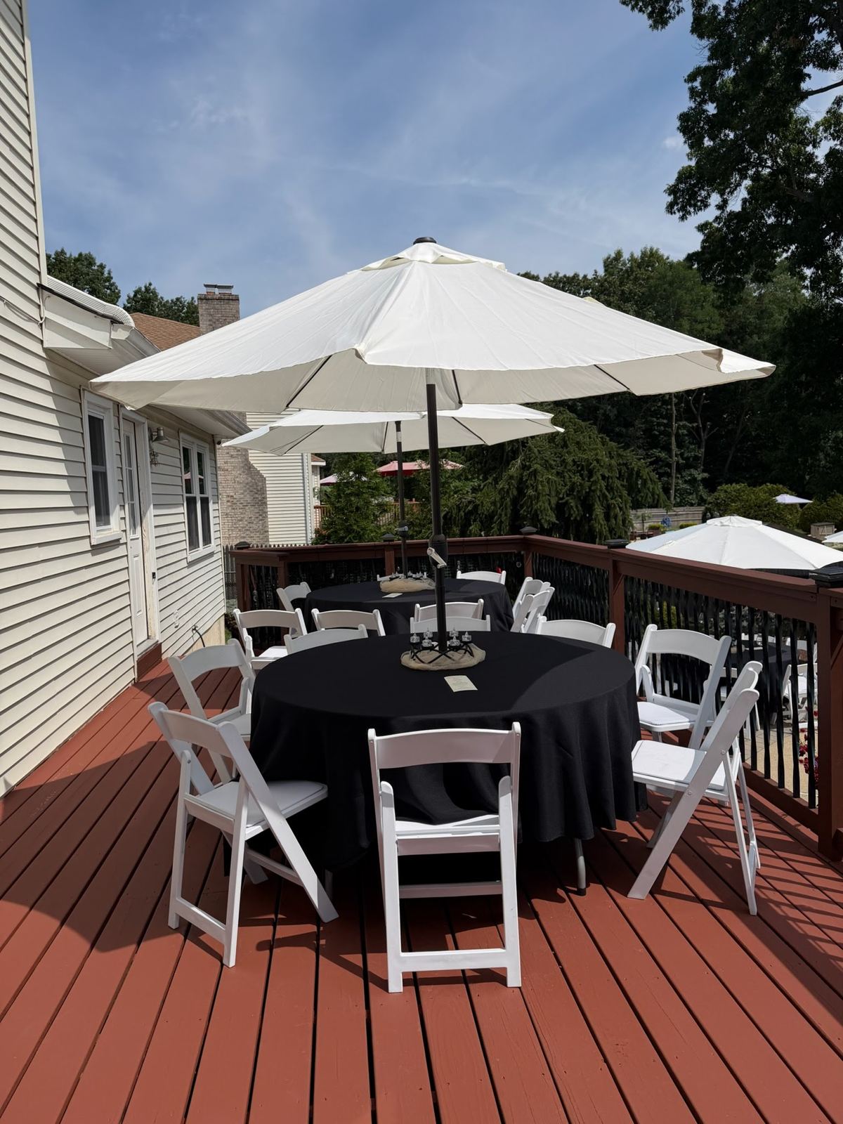 Black linens and white padded chairs under umbrellas on a deck
