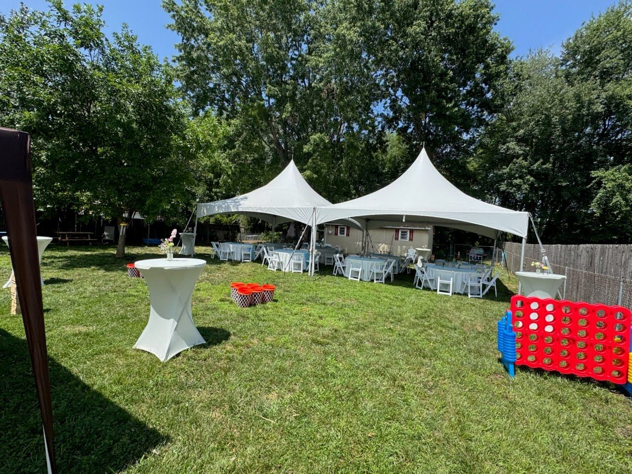Two high-peak tents with cocktail tables and giant Connect 4 on the lawn